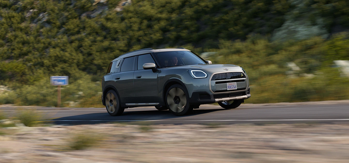 A tisztán elektromos MINI Countryman oldalnézete, Smokey Green színben, Vibrant Silver színű tetővel.