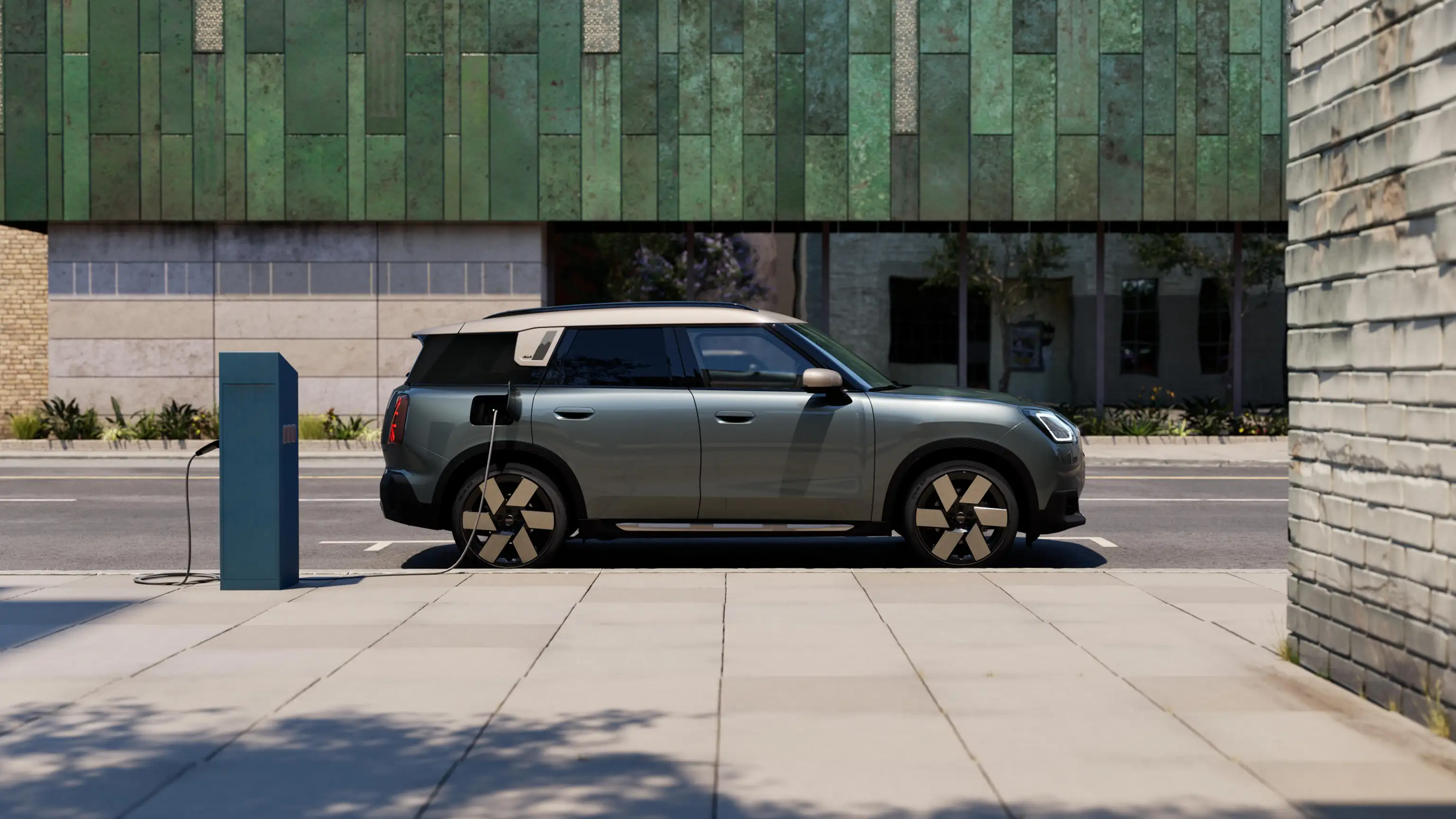 Egy Smokey Green fényezésű, Vibrant Silver tetővel rendelkező, tisztán elektromos MINI Countryman utcai töltése oldalnézetből