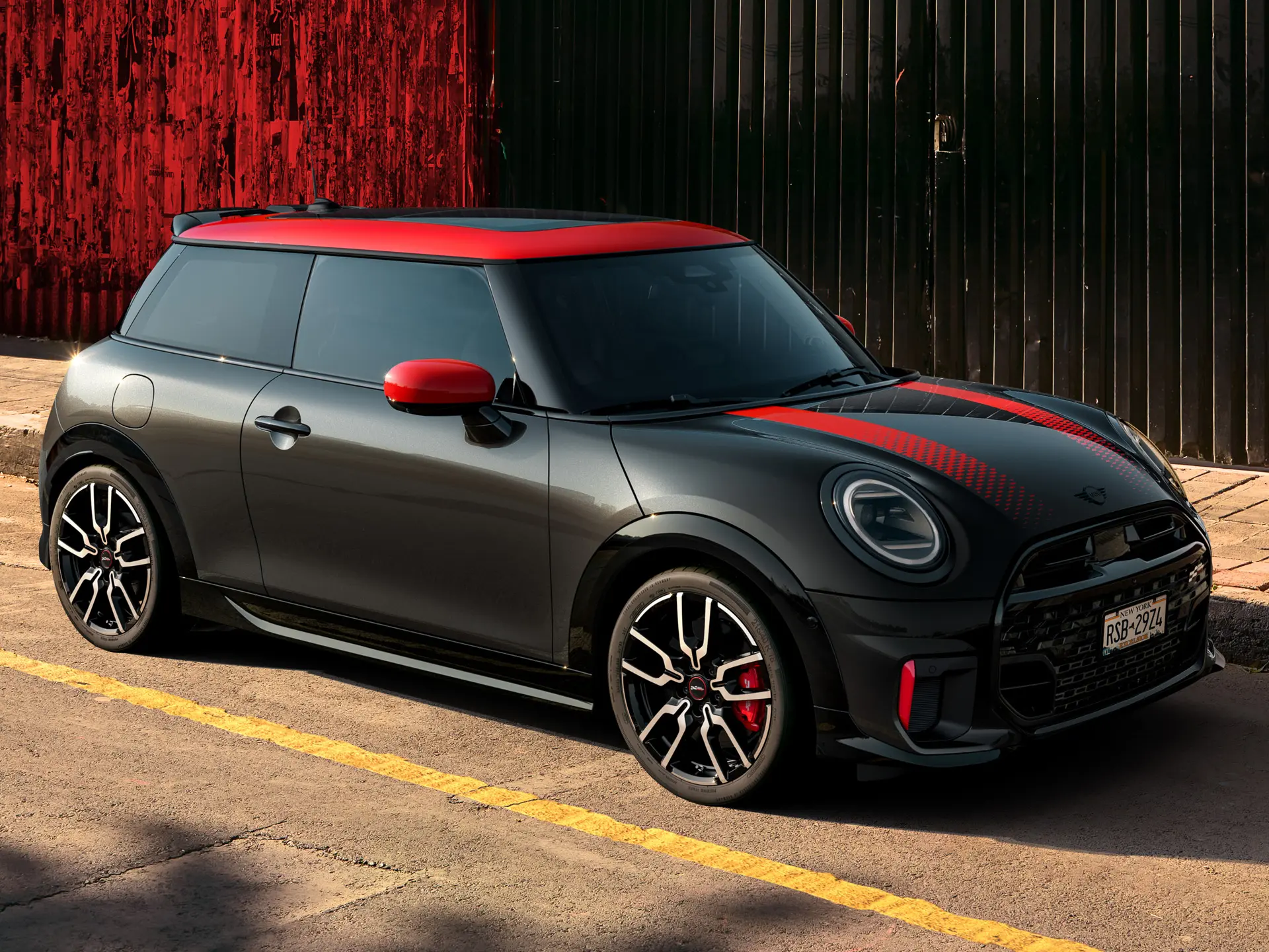 Egy Midnight Black fényezésű, Chili Red színű tetővel és tükörburkolatokkal, valamint vörös sportcsíkokkal ellátott, az utcán parkoló 3 ajtós MINI John Cooper Works oldalról.