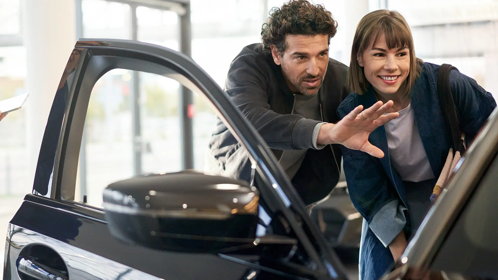 Egy MINI márkakereskedésben álló MINI, amely mellett egy értékesítési tanácsadó magyarázza egy vevőnek a belső funkciók működését.