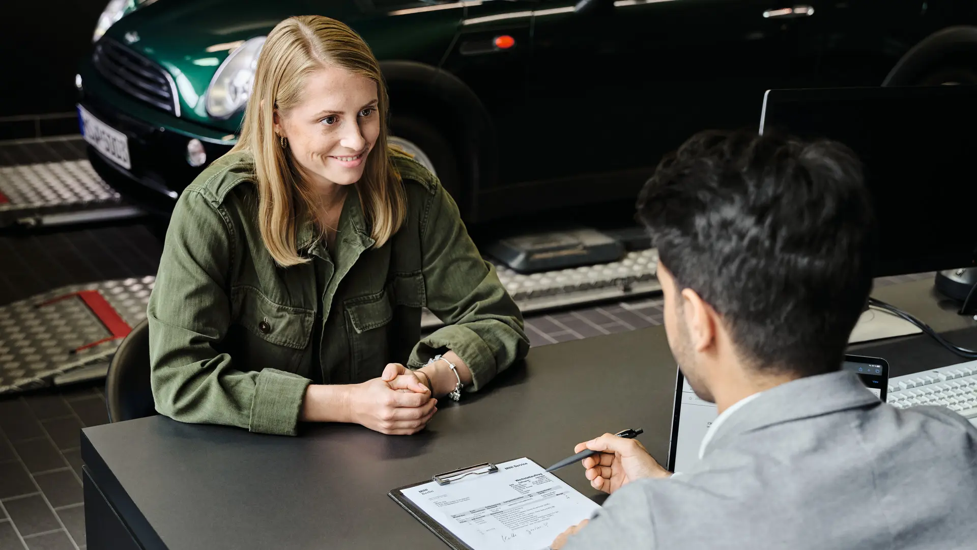 A MINI márkakereskedés tanácsadója asztal mellett ülve egy ügyfelet tájékoztat a szervizelési lehetőségekről.